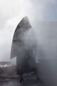 Tourist with towel posing as surreal figure in the geyser mist El Tatio Geysers, Atacama Desert, Chile